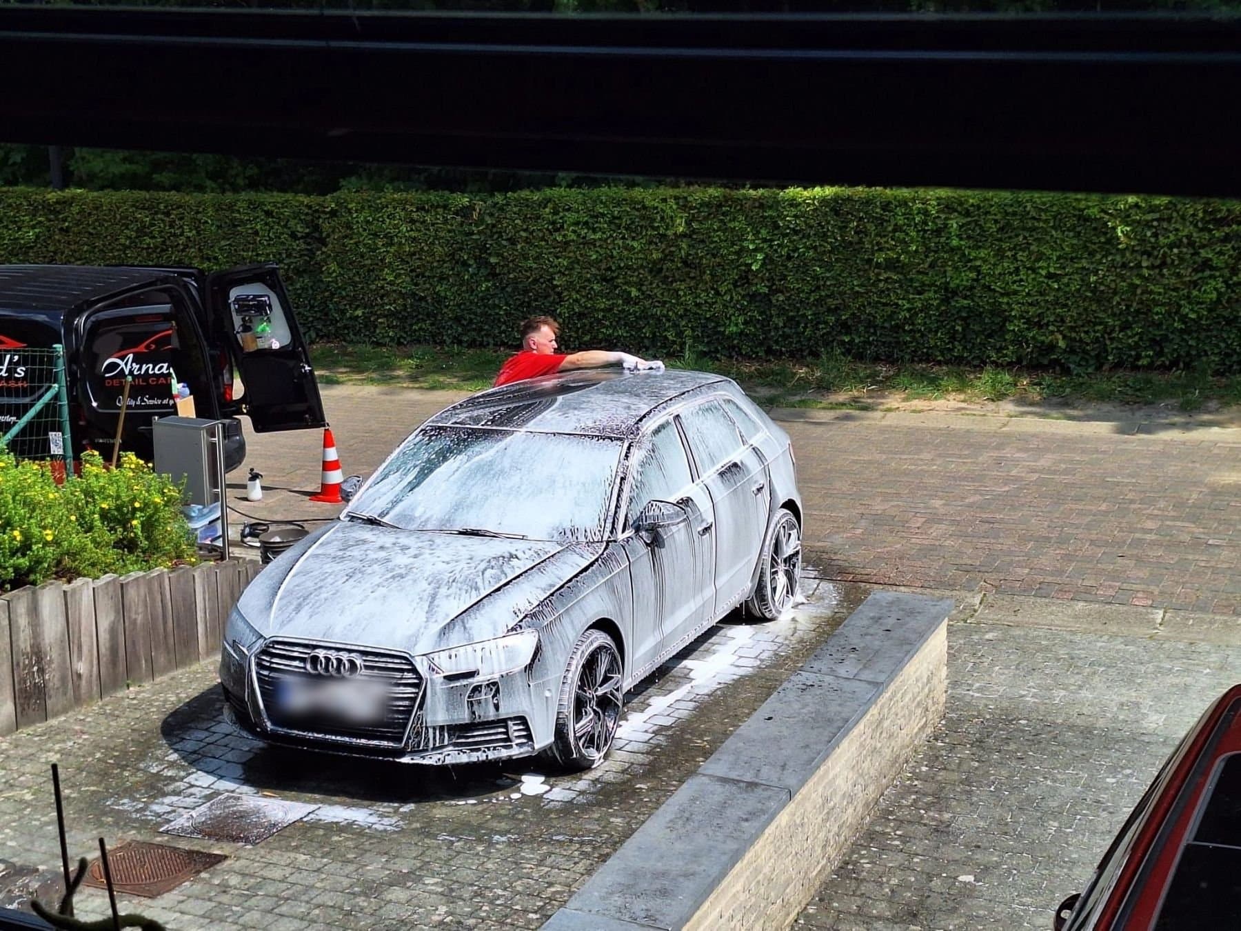 Arnaud wast een wagen met de hand op een oprit, naast de bestelwagen